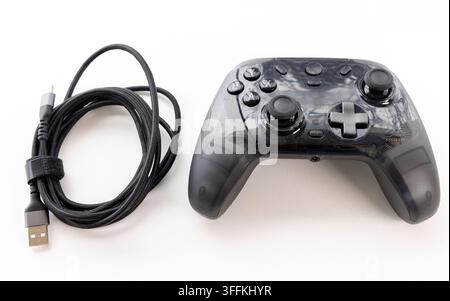 A transparent black game controller and coiled USB cable rest on white Stock Photo