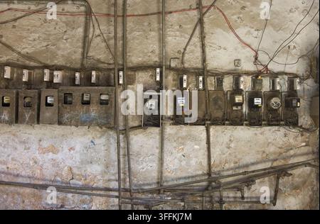 View of old electricity meters mounted on a weathered concrete wall with exposed wiring and pipes in Havana, Havana, Cuba. Stock Photo