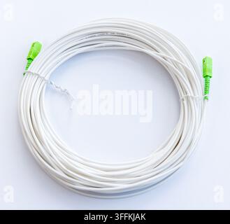 A white coiled fiber optic cable with green connectors rests on a white background Stock Photo