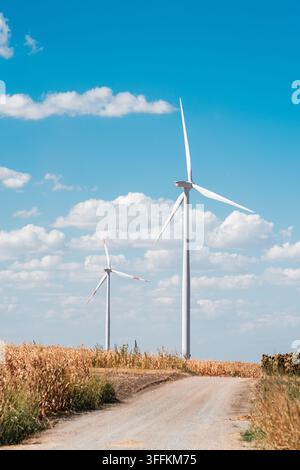View of Wind farm Alibunar with tall white wind turbines standing in a dry corn field next to a dirt road under a clear blue sky in Alibunar, Vojvodin Stock Photo