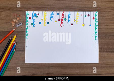 Blank watercolor paper on wooden desk with colorful hanging ribbon doodles, round ornaments, and colored pencils for crafting Stock Photo