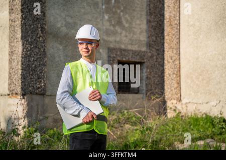 Construction professional holding paperwork outside an unfinished building site. Project management compliance inspection and construction documentati Stock Photo
