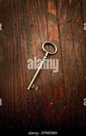 Old metal key lying diagonally on dark weathered wooden boards, a rustic still life suggesting access, secrecy, history and discovery Stock Photo