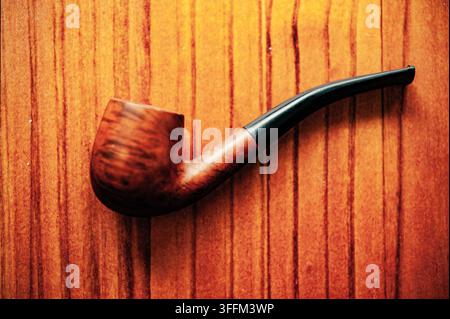Classic wooden smoking pipe with a curved black stem on a warm wood surface, photographed as a simple vintage-style still life Stock Photo