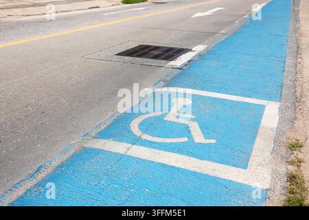 Blue accessible pathway marking runs along pavement edge, wheelchair symbol guides pedestrians toward safe route designed for people with disabilities Stock Photo