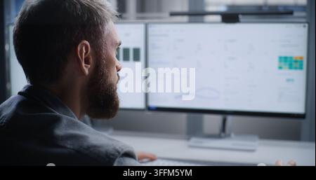 Data Center Technician Monitors Server Systems After Critical Overheating Alert, Analyzing Systems on Dual Screens to Resolve Issues, Protect Hardware Stock Photo