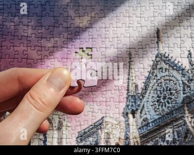 Hand inserting final missing piece into cathedral architectural jigsaw puzzle Stock Photo