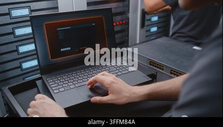 Male IT Engineer Handles DDoS Alert Using Linux Command Line, Reviewing Network Conditions and Performing Emergency Troubleshooting While Monitoring C Stock Photo