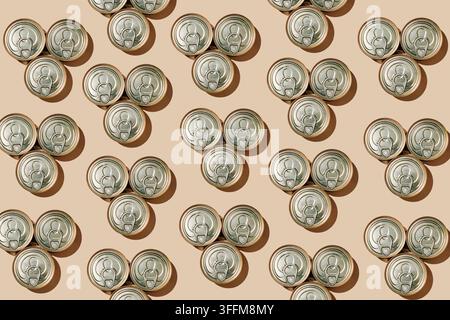 repeating triangular groups of three unopened food cans with ring pull lids create a geometric pattern on a beige background, with crisp shadows outli Stock Photo