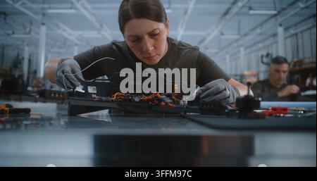 Young Female Specialist Wearing Protective Gloves Uses Precision Screwdriver Assembling FPV Drone Frame. Focused Woman Connects Electronic Flight Cont Stock Photo