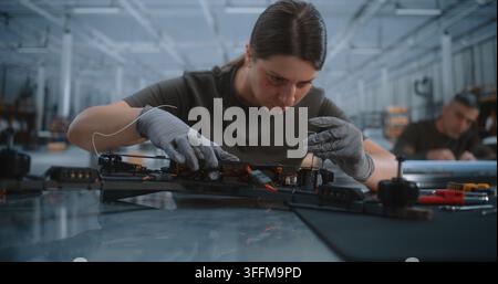 Young Female Specialist Wearing Protective Gloves Uses Precision Screwdriver Assembling FPV Drone Frame. Focused Woman Connects Electronic Flight Cont Stock Photo