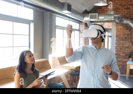 Diverse coworkers demonstrating VR headset interaction in coworking office with tablet and stylus Stock Photo