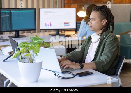 African American coworkers typing and analyzing code on laptop with monitors, smartphone, plant Stock Photo