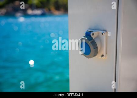 Electrical power outlet mounted on Electric charging station for boats near a turquoise sea with blurred boats in the background, Milna, Croatia Stock Photo