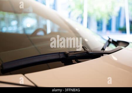 Detailed close up shot of black windshield wipers resting at the base of a clean car windshield hood line on a white modern automobile. Stock Photo