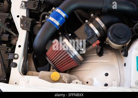 High angle detailed shot showing an aftermarket performance red cone air filter connected to intake piping inside a white vehicle engine compartment. Stock Photo
