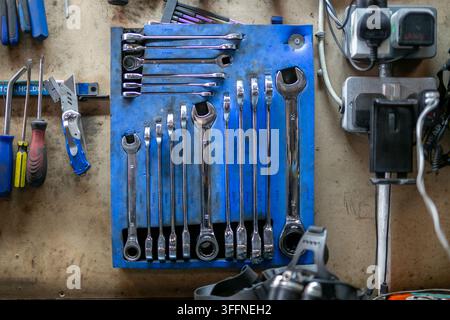 Collection of chrome combination spanners, also known as wrenches, neatly arranged in a vertical wall-mounted organiser rack inside a car workshop Stock Photo