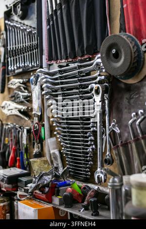 Collection of chrome combination spanners, also known as wrenches, neatly arranged in a vertical wall-mounted organiser rack inside a car workshop Stock Photo