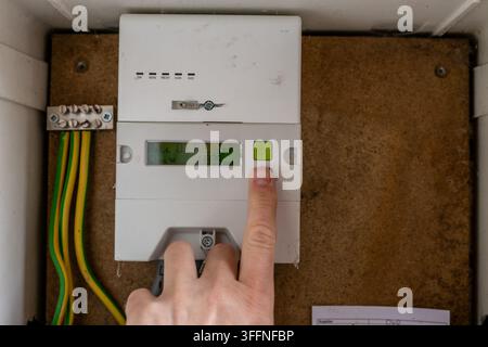 Person pressing a button on a residential electricity meter to check or access information displayed by the meter. The close-up illustrates household Stock Photo