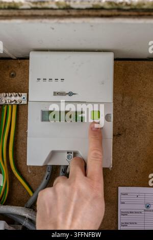 Person pressing a button on a residential electricity meter to check or access information displayed by the meter. The close-up illustrates household Stock Photo
