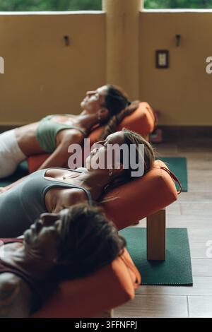 Group of women lying on yoga bolsters in a studio, practicing relaxation Stock Photo