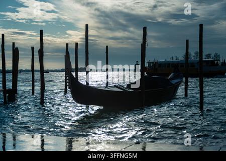 A classic Venetian gondola, resting on wooden stakes (the so-called Bricole) in the Venice lagoon, illuminated by the setting sun. Stock Photo