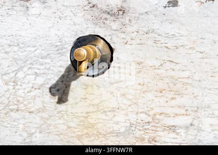 Close-up of a traditional brass wall faucet mounted on a weathered white marble surface. The polished metal fixture contrasts with the textured stone, Stock Photo