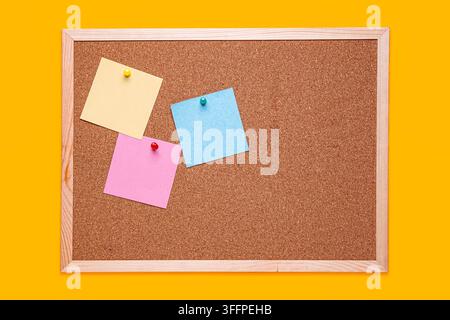 Cork notice board with colorful sticky notes pinned on a bright yellow background. Stock Photo