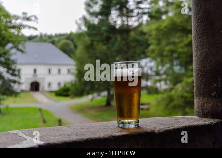 Glass of cold golden beer standing on stone wall with distant castle background, refreshing beverage, travel concept. Stock Photo