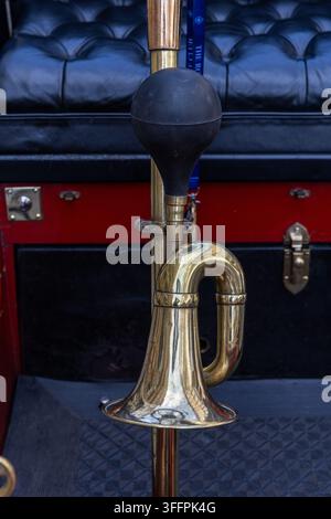 Shiny brass horn mounted on carriage with black leather upholstery and red trim. Stock Photo