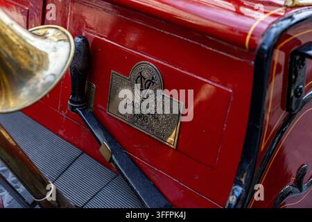 Close-up of 1903 Cadillac plaque on red vintage car body with brass horn and black handle. Stock Photo