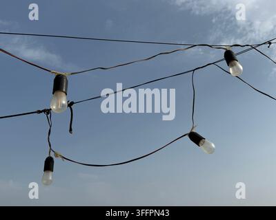 String lights and tangled overhead wires against a blue sky, a conceptual image of connection and networks Stock Photo