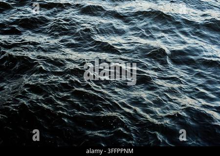 Close-up view of dark ocean water with rippling waves, deep blue tones, and shifting highlights. Natural sea surface texture creates a dramatic abstra Stock Photo