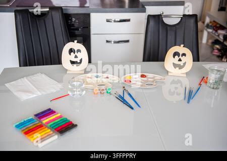 Halloween DIY craft setup on a kitchen table with wooden pumpkin decorations, paint palettes, brushes, markers, water jars and napkins prepared for cr Stock Photo