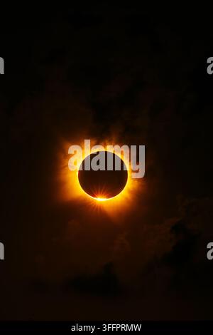 Dramatic close view of a total solar eclipse, with the Moon silhouetted against the Sun’s glowing orange corona and a brilliant diamond ring flare in Stock Photo