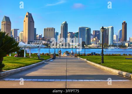 The San Diego skyline rises above the bay with lush green grass and walking paths in Coronado Park. Urban buildings and waterfront scenery combine wit Stock Photo