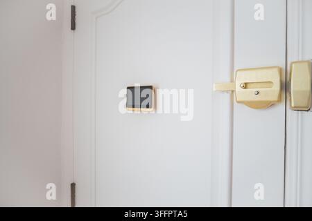 Close-up of a white apartment door with a gold smart lock and wall-mounted digital control panel, illustrating modern home security, access technology Stock Photo
