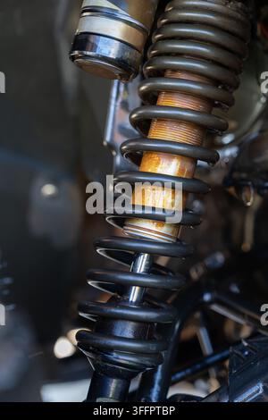 Close-up of a motorcycle suspension system showing a black coil spring, shock absorber, metal linkage, and worn mechanical components in a detailed ve Stock Photo