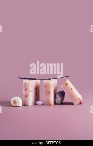Handmade lavender soap bars, seashell, polished crystal and botanical sprigs form a refined horizontal still life on a soft pink pastel background for Stock Photo