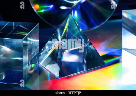 Abstract futuristic composition of glass prism shapes and crystal blocks reflecting vivid rainbow light across a dark surface, creating a luminous tec Stock Photo
