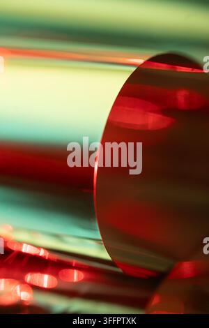 Close-up abstract view of a reflective metal cylinder illuminated by vivid red and green light, creating glossy highlights, soft blur, and a modern in Stock Photo
