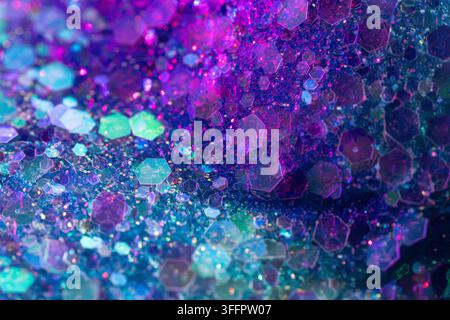 Abstract macro background of sparkling hexagonal glitter particles in vibrant purple, blue, pink, and teal tones, creating a luminous festive texture Stock Photo