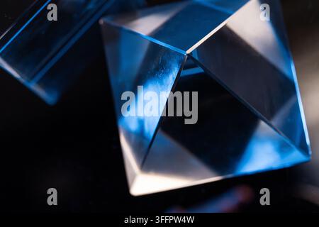Abstract close-up of transparent geometric glass prisms refracting blue light against a dark background, creating sharp reflections, luminous facets, Stock Photo