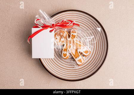 Overhead view of a homemade Christmas gingerbread cookie decorated with white icing, wrapped in cellophane with a red ribbon and blank gift tag on a r Stock Photo