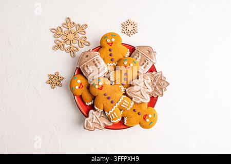 Festive homemade Christmas gingerbread cookies arranged on a red plate with iced house and snowflake treats, surrounded by rustic wooden snowflake dec Stock Photo