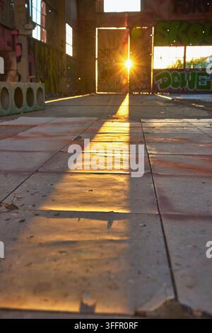 Golden hour sunlight streams through a doorway in the abandoned Goldome Mill in California casting a dramatic sunburst across graffiti walls and dusty Stock Photo
