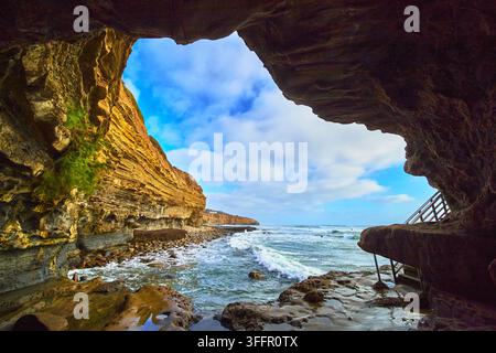 A stunning view from inside a natural cave at Sunset Cliffs in San Diego California reveals the vibrant ocean the rugged beach and the sweeping sky. T Stock Photo