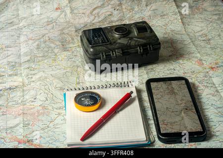 Wilderness exploration planning with map, compass, smartphone, and trail camera Stock Photo
