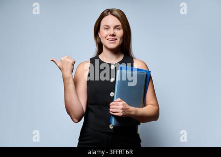 Businesswoman holding folders pointing thumb aside on grey background Stock Photo