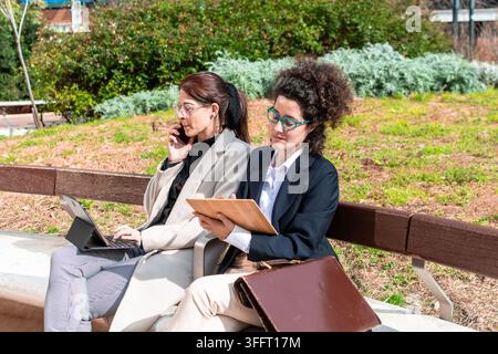 Businesswomen collaborating outdoors on park bench Stock Photo